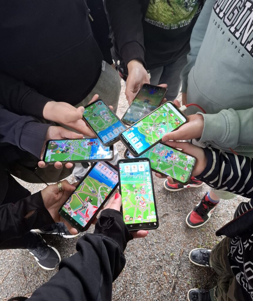 Kuvassa ihmisiä ringissä pitämässä kännyköitä käsissään. Kännyköiden näytöillä Pokemon go -peli.